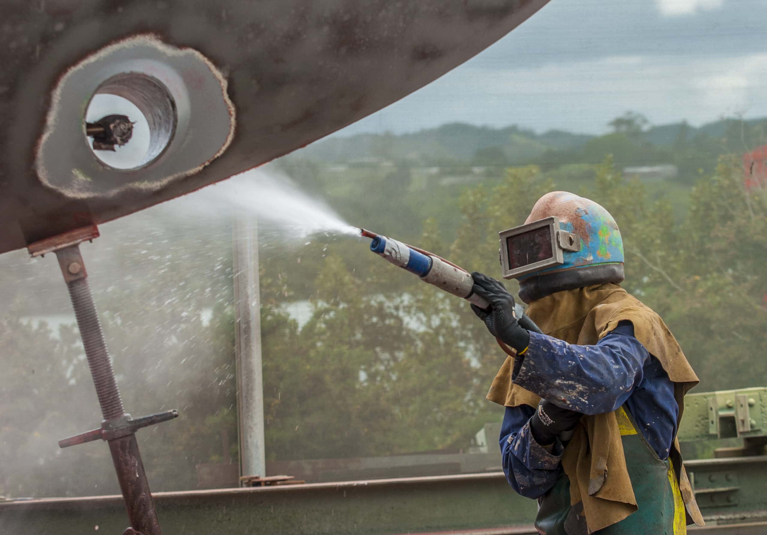 worker, sandblasting the corroded hull of a sailing vessel with a high pressure sandblasting system