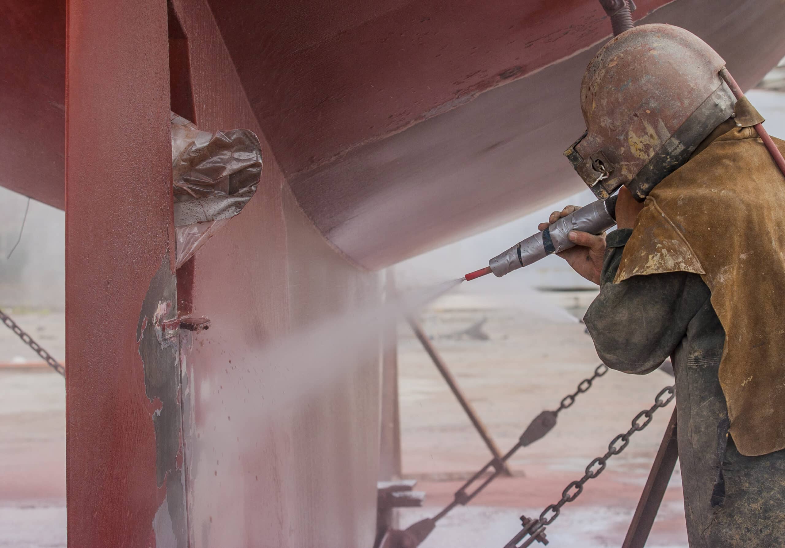 worker, sandblasting the corroded hull of a sailing vessel with a high pressure sandblasting system